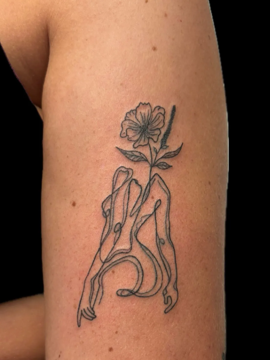 Fine line bloem met abstracte lijntekening op de bovenarm, tattoo Gent