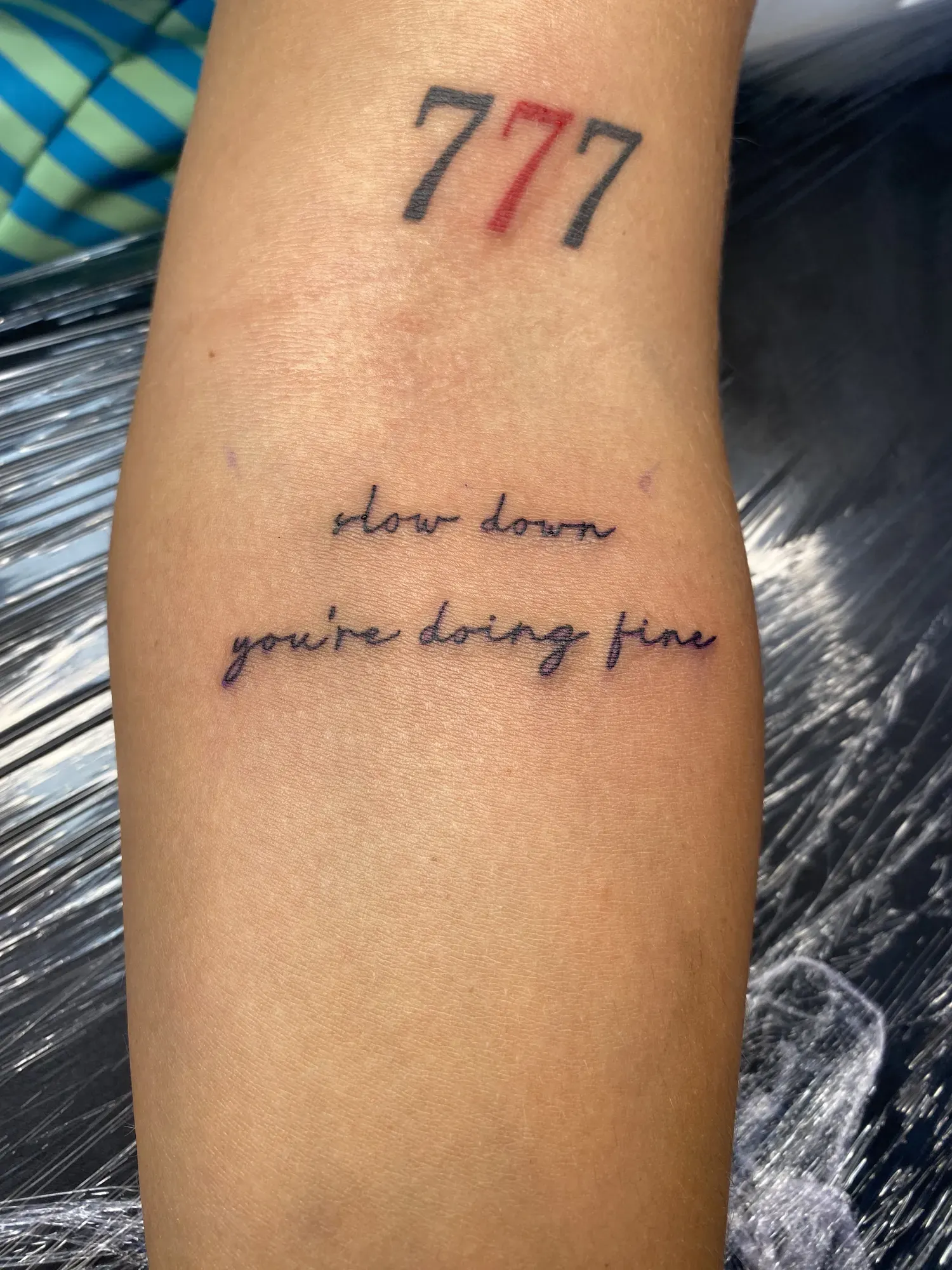 Lettering 777 met de tekst slow down you're doing fine op de onderarm, tattoo Gent